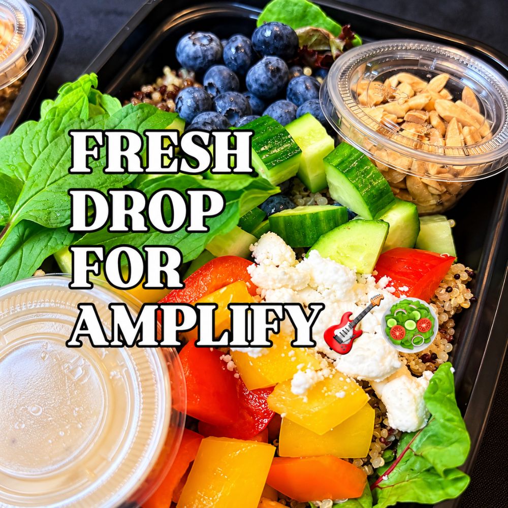 Fresh salad bowl with spinach, blueberries, cucumber, quinoa, colorful bell peppers, vegan cheese, and dressing containers, with text reading ‘Fresh Drop for Amplify.